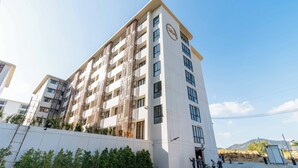 A multi-story hotel with a modern design, featuring balconies on each floor and a prominent logo on the facade. - 1BR w Pool Gym near Nai Harn C266 (Rawai)