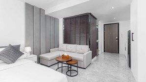 A modern hotel room with a large bed, a sofa, a small round table, and a dark wooden partition. - 1BR w Pool Gym near Nai Harn C266 (Rawai)