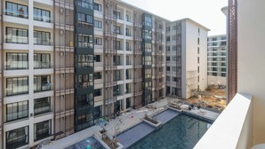 A multi-story residential building with balconies, a swimming pool, and a construction site. - 1BR w Pool Gym near Nai Harn C266 (Rawai)