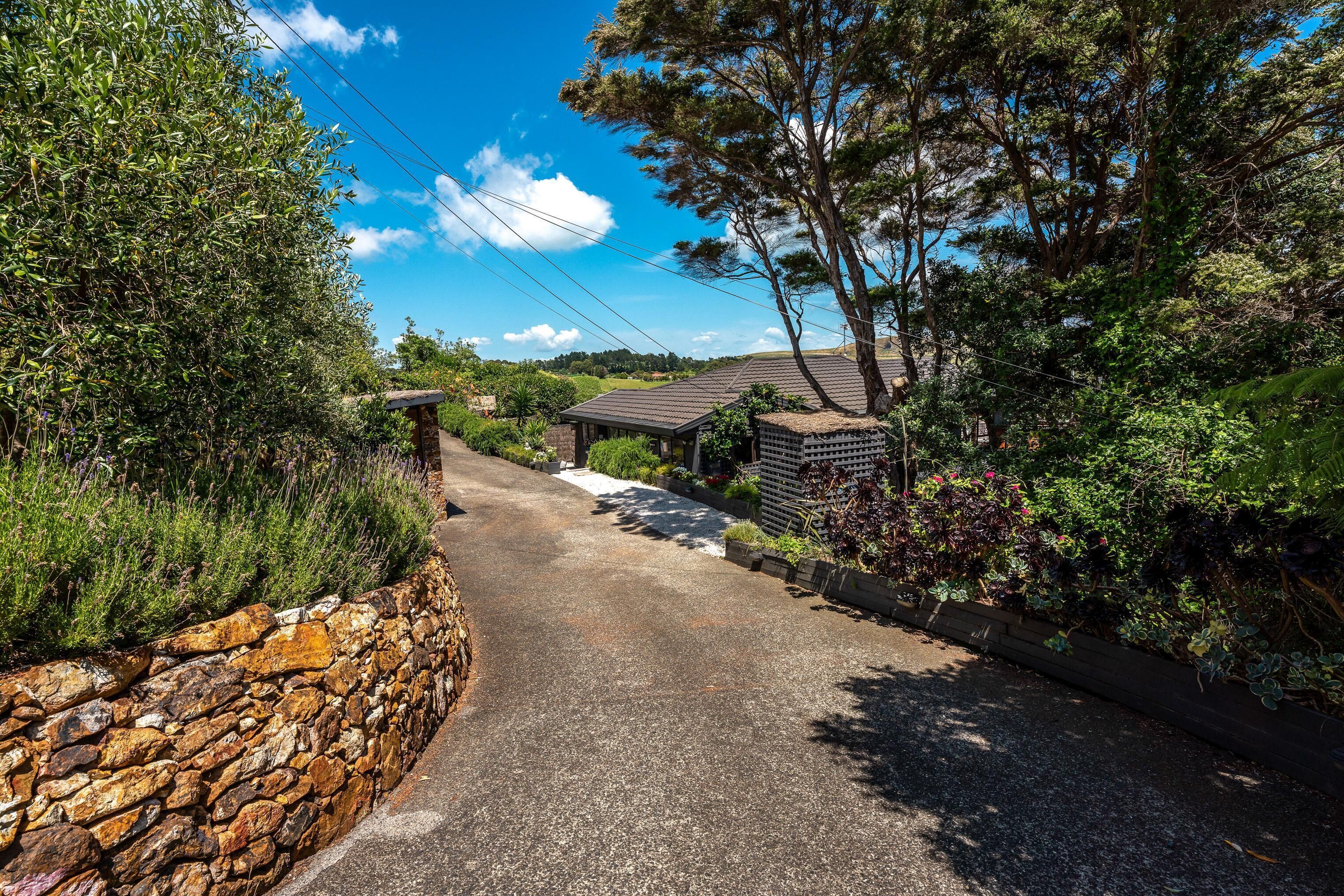 Un chemin de campagne menant à un mur de pierres et à une maison avec un toit en pente.