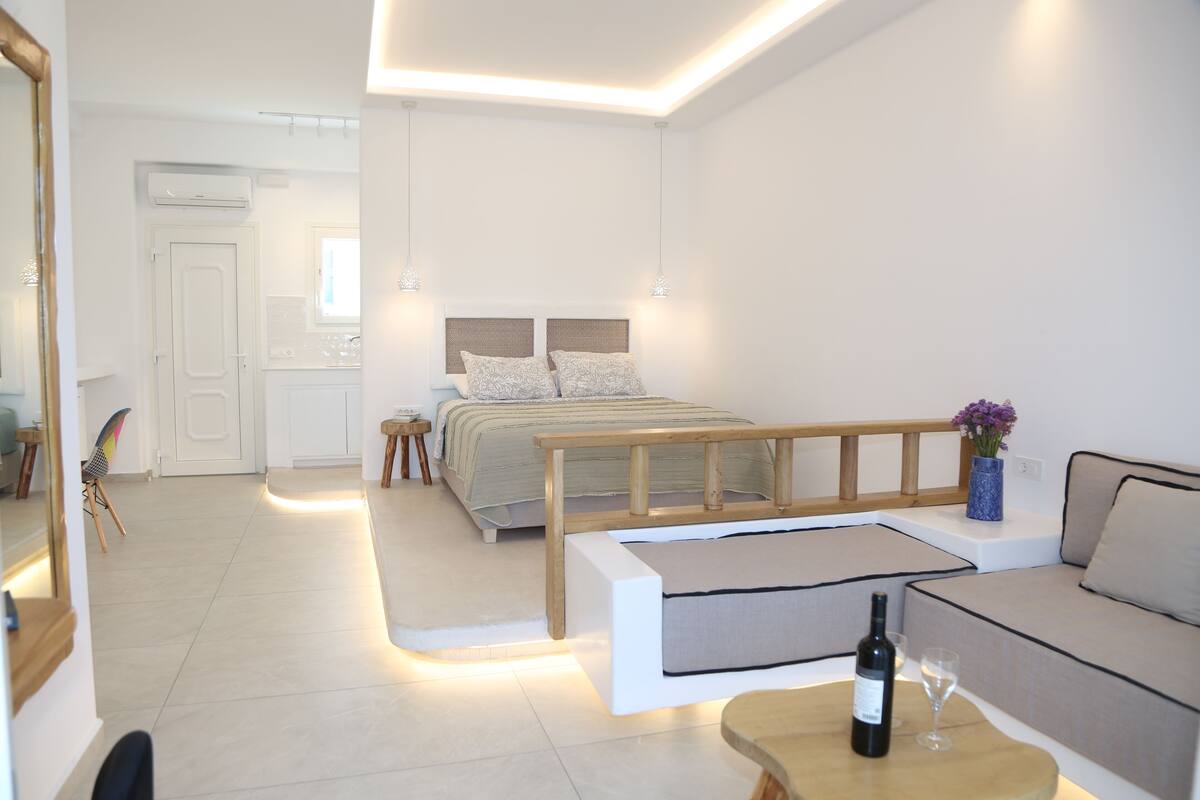 A modern bedroom with a bed, bedside tables, a sofa, and a small table with a bottle and glass.