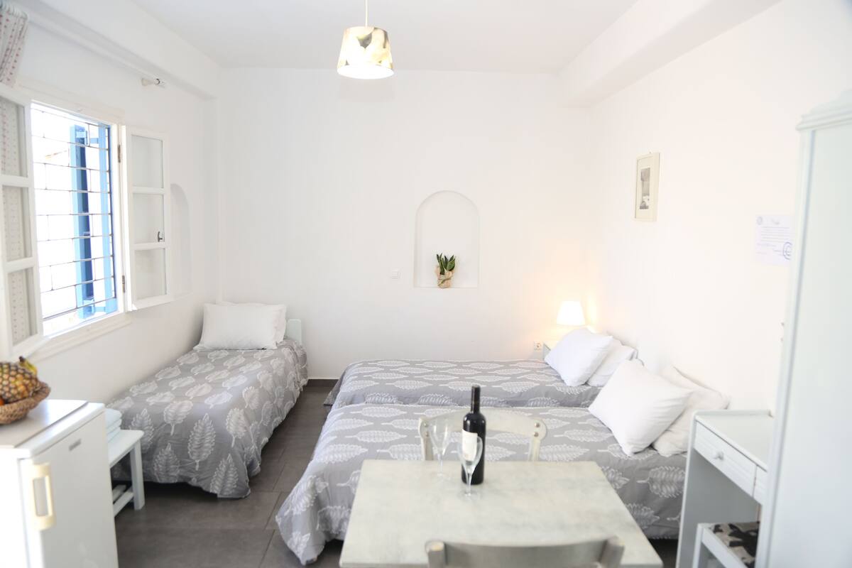 A clean, well-lit room with two beds, a dining table, and a small kitchen area.