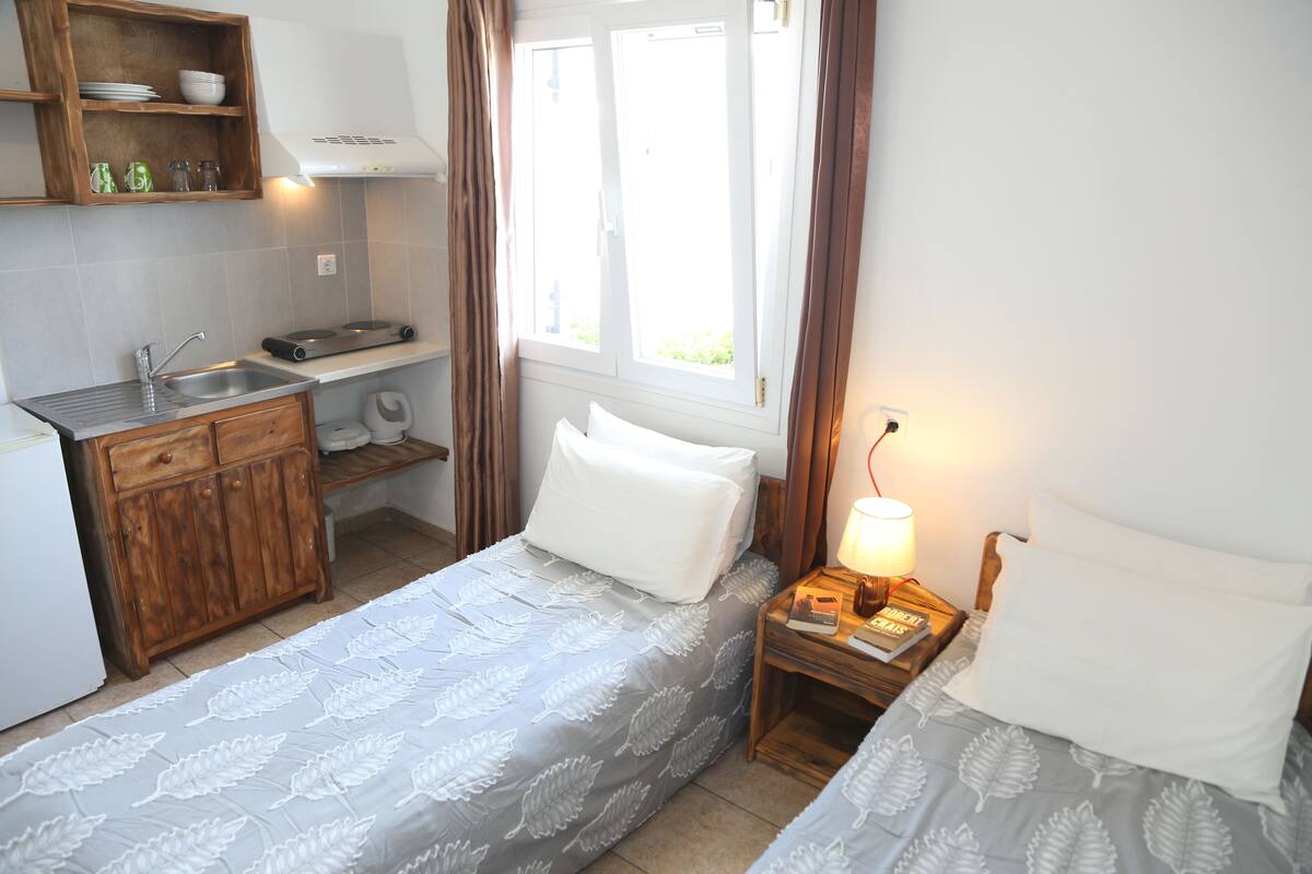 A compact bedroom with two beds, a small kitchenette, and a window providing natural light.