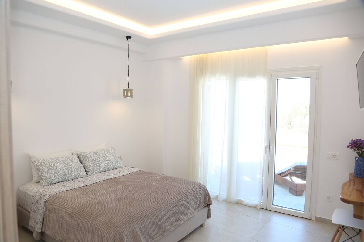 A bedroom with a bed, a ceiling light, a sliding glass door, and a small table with a vase.