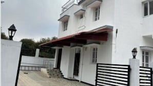 Une maison blanche à deux étages, avec un toit rouge, une entrée fermée par un portail et une allée pavée.