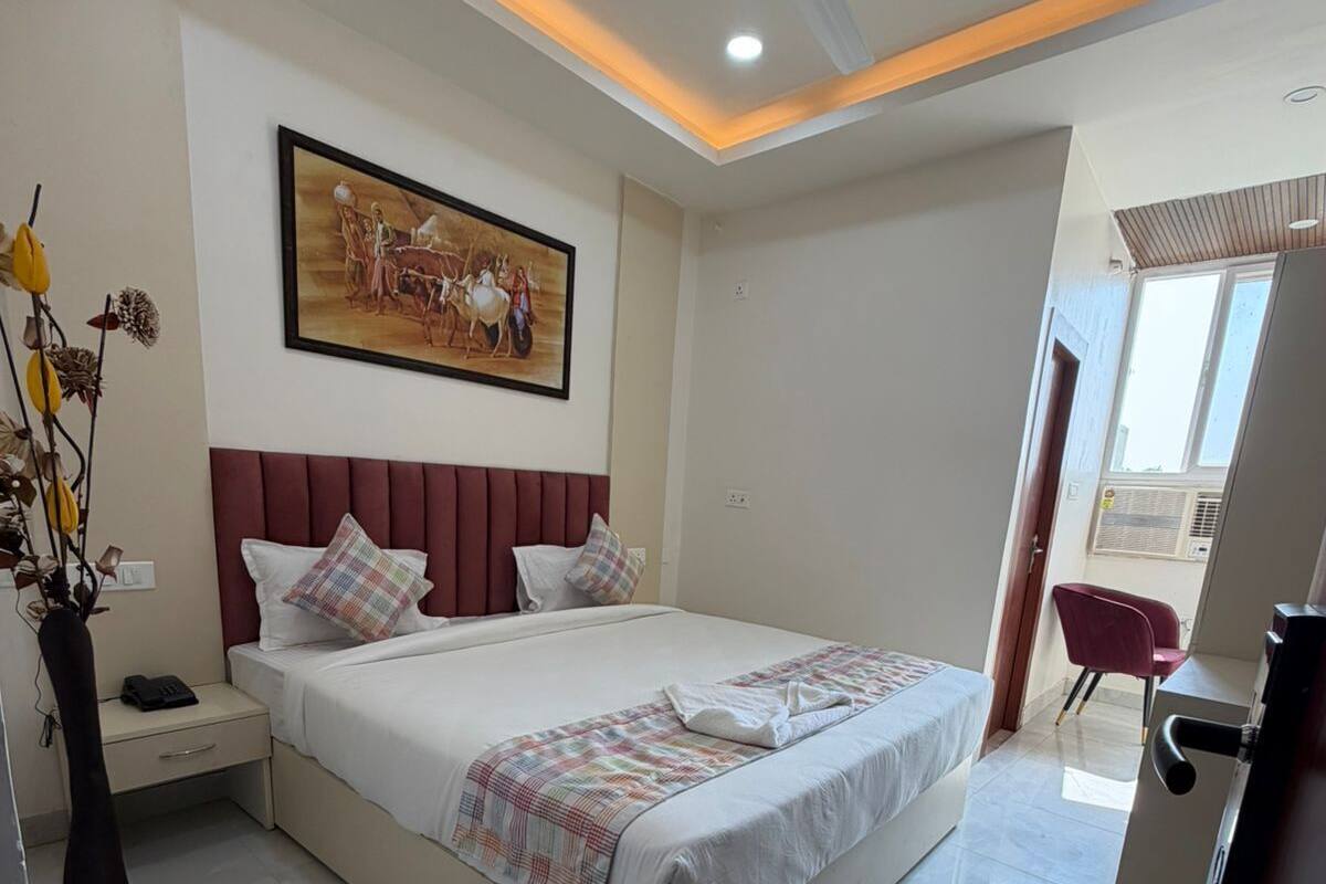 A modern bedroom with a large bed, a ceiling fan, recessed lighting, a painting on the wall, and a view of the outside through a window.