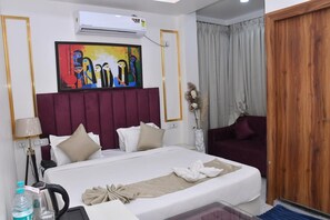 A hotel room with a bed, a painting, an air conditioner, a sofa, and a wooden door. - Bisaka Hotel (Patna)
