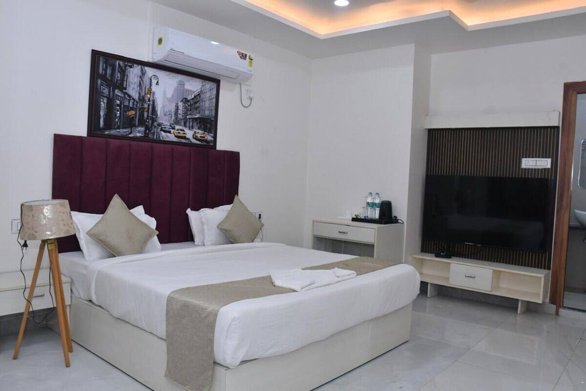 A modern hotel room with a large bed, a flat-screen TV, a bedside table, and an air conditioning unit.