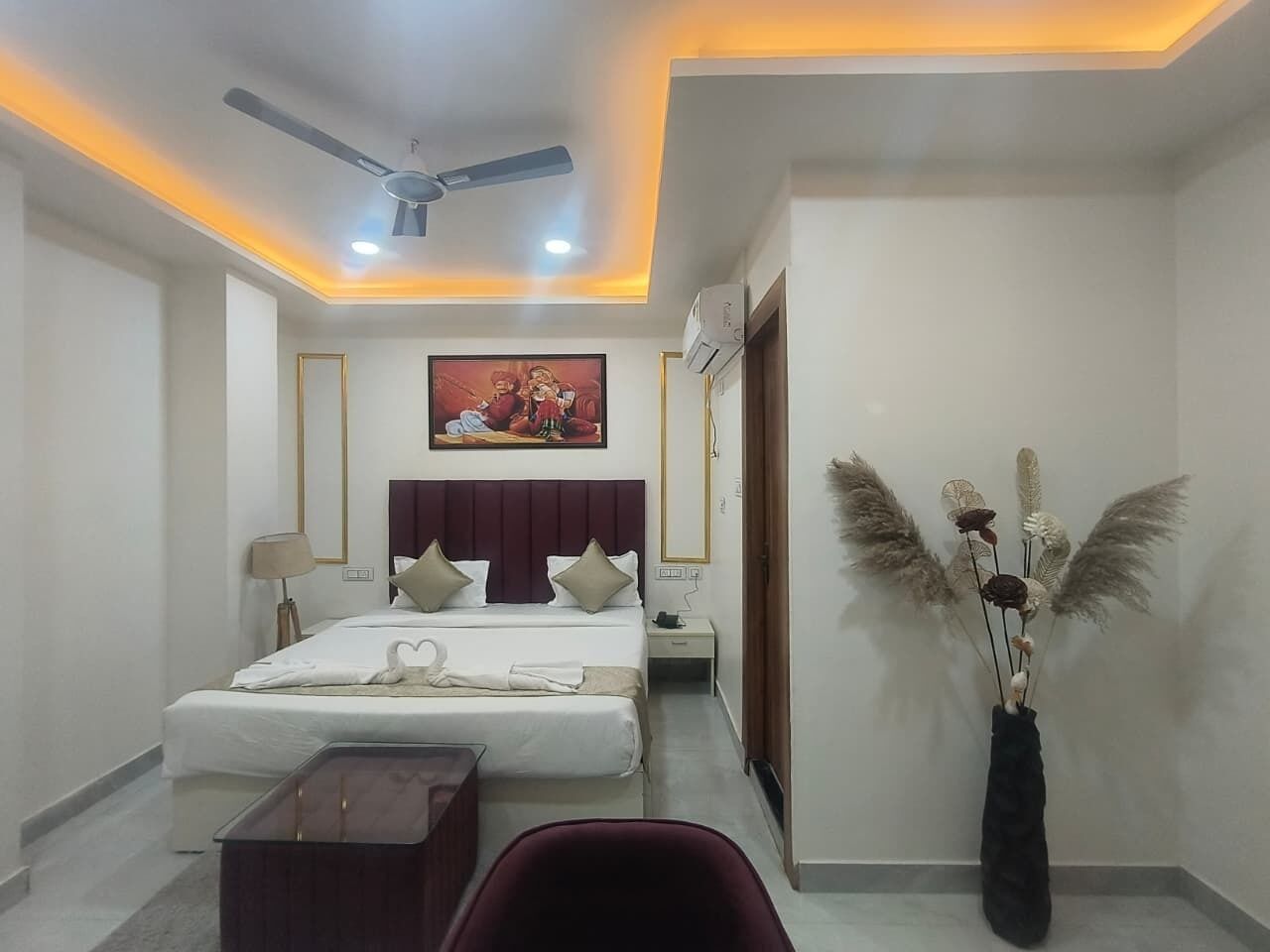Una habitación de hotel moderna con cama, mesitas de noche, ventilador de techo y un jarrón decorativo con plumas de pampa.