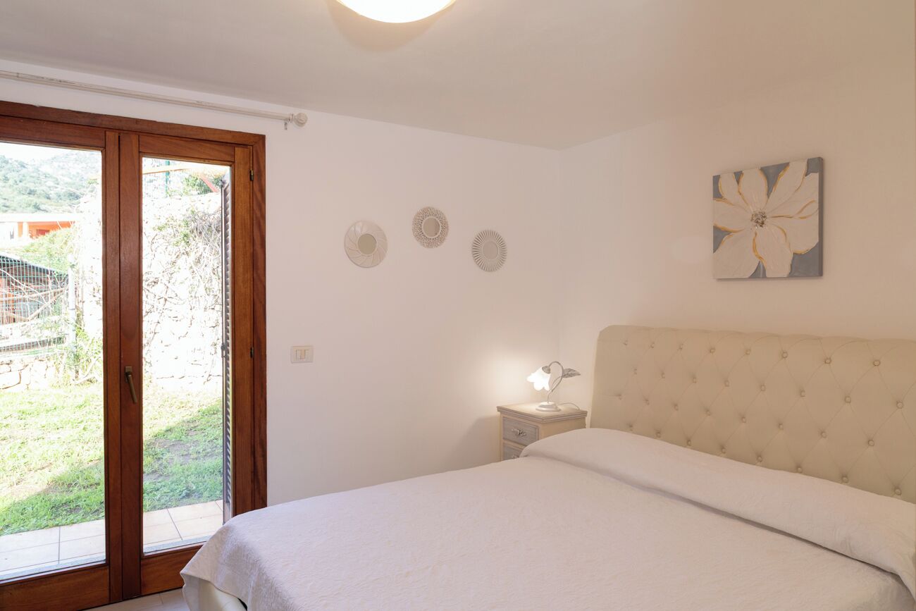 Une chambre avec un lit, une table de chevet avec une lampe, une porte-fenêtre coulissante donnant sur un jardin et un mur orné de trois éléments décoratifs circulaires.