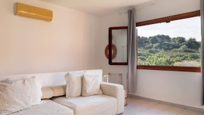 A modern living room with a white sofa, a large window with a view of greenery, and a wall-mounted air conditioner. - Casa Leo by Wonderful Italy (Osseddu)