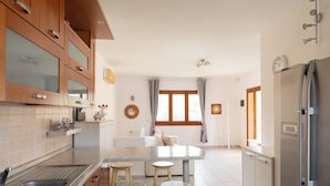 A modern kitchen with wooden cabinets, a marble countertop, and a built-in sink. There are three stools at the kitchen island. - Casa Leo by Wonderful Italy (Osseddu)