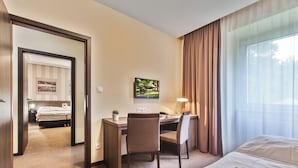 Habitación de hotel con cama, escritorio, silla y un gran ventanal con cortinas.