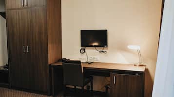 Ett hotellrum med ett skrivbord i trä, en stol, en tv som är monterad på väggen och en lampa.