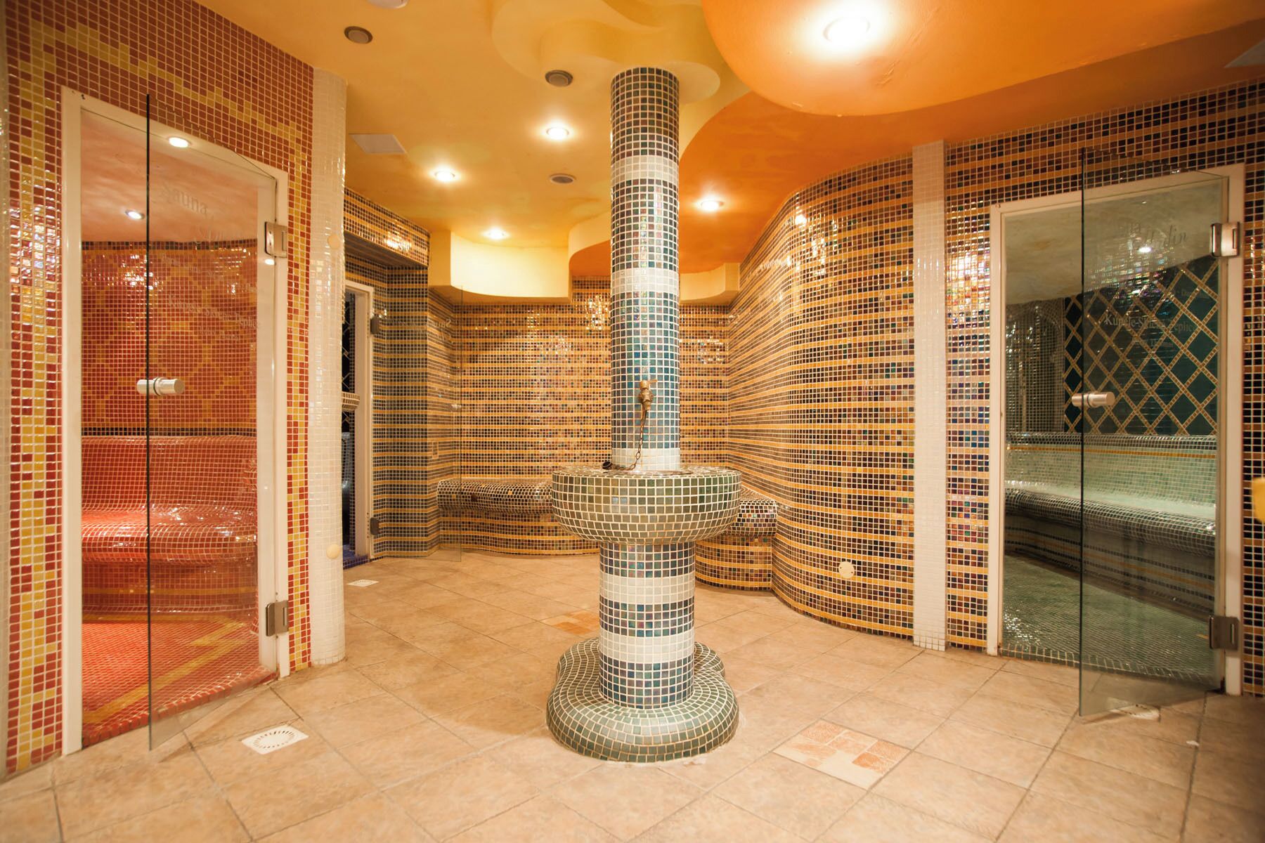 A spa area with mosaic walls, a central column, and a glass-enclosed shower.