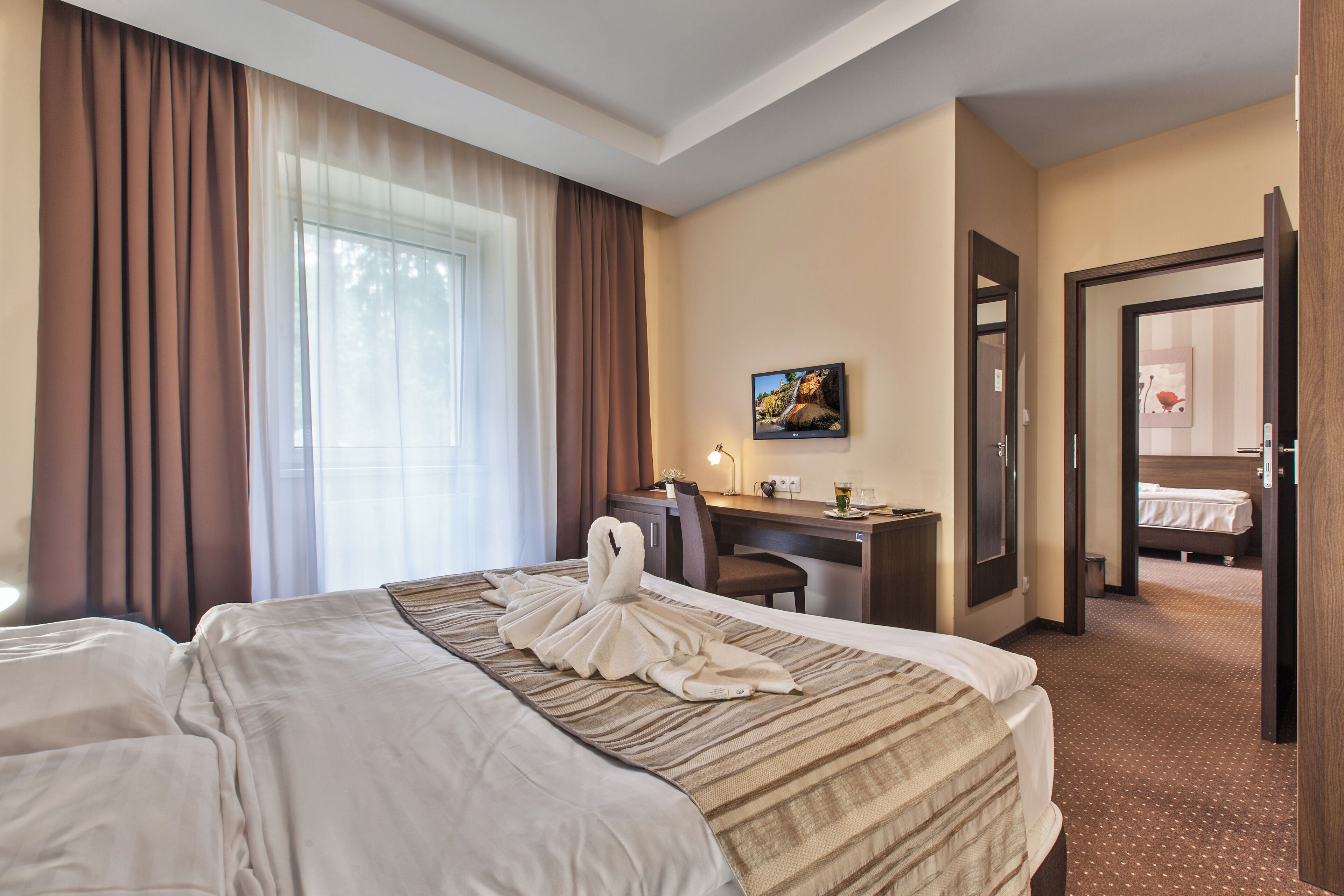 A hotel room with two beds, a desk, a chair, a painting, and a door leading to another room.