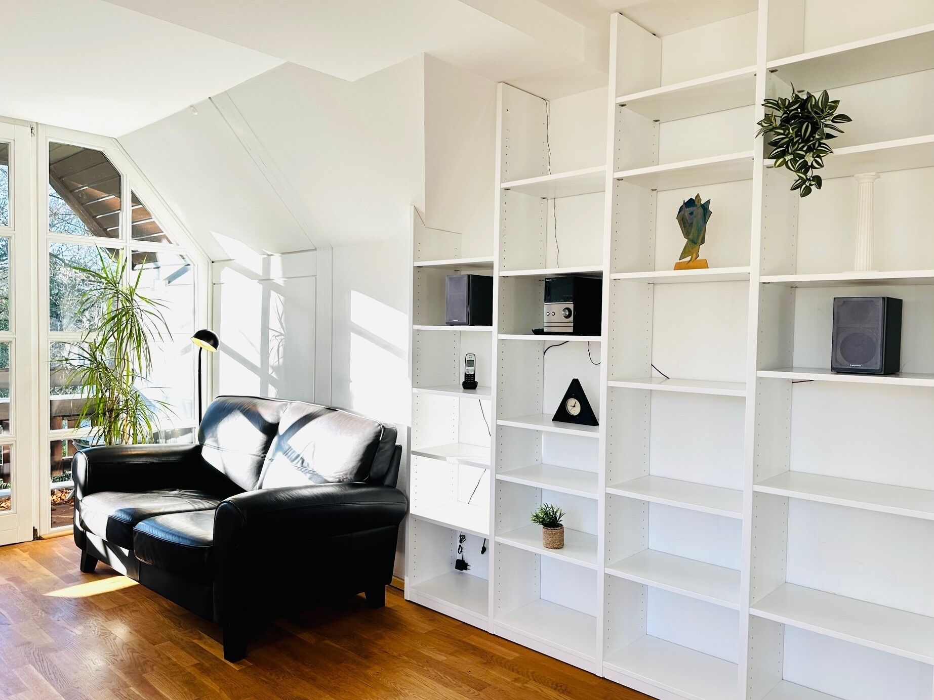 Ein modernes Wohnzimmer mit einem schwarzen Ledersofa, weißen Regaleinheiten und einer Treppe, die in einen oberen Bereich führt.