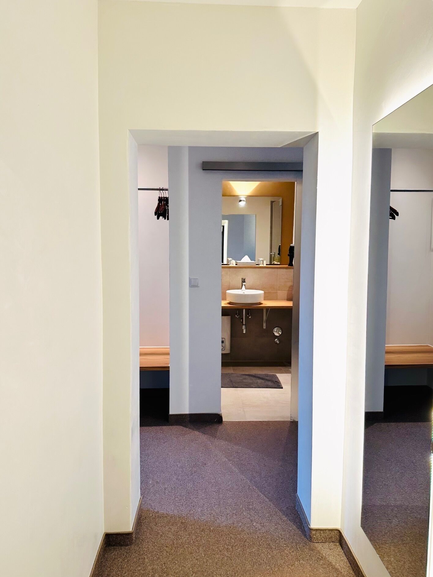 A hallway leading to a bathroom with a sink and mirror.