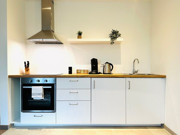 Una cocina moderna con horno integrado, campana extractora de acero inoxidable, cafetera y pileta.