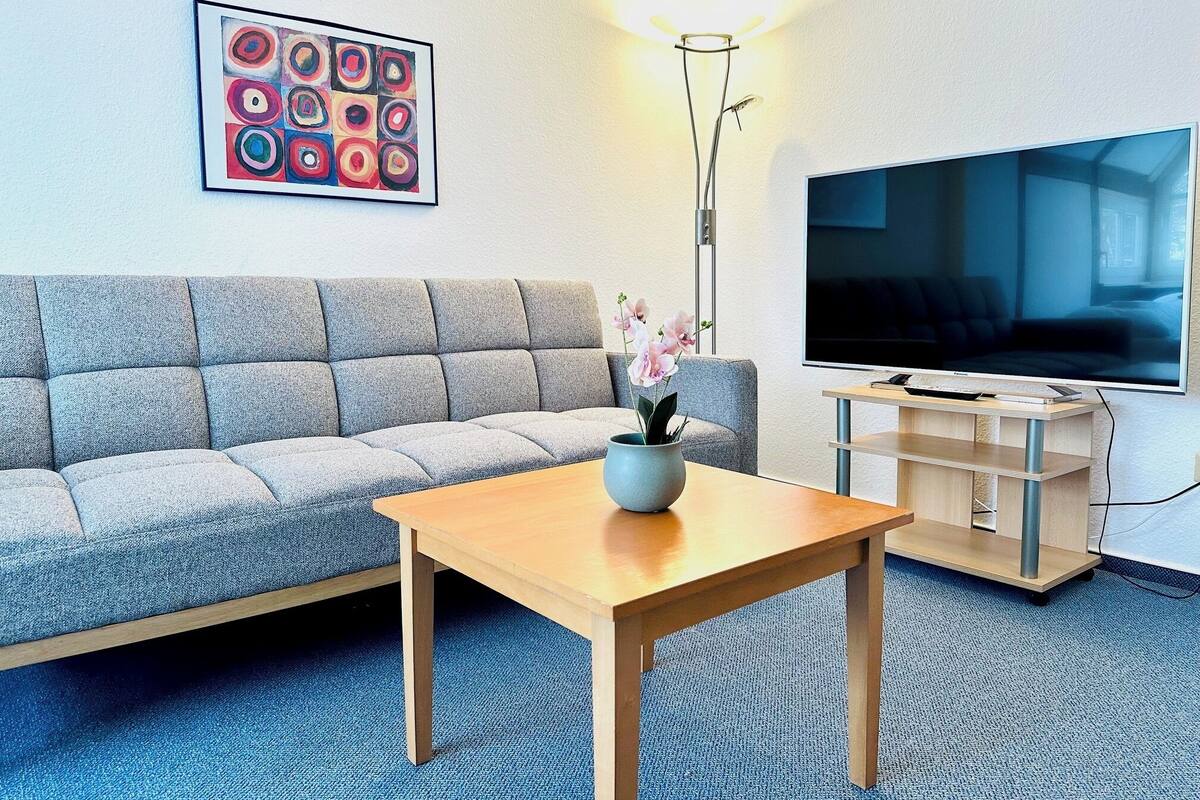 A modern living room with a grey sofa, a wooden coffee table, a TV, and a floor lamp.