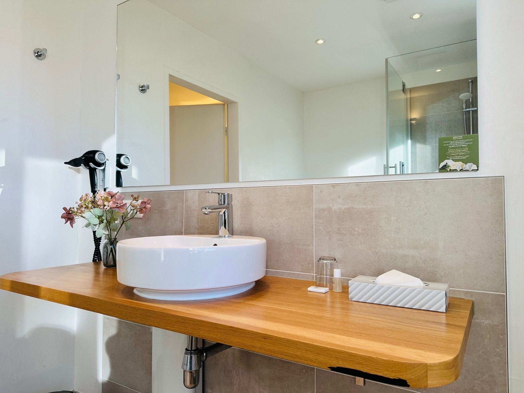Une salle de bain moderne avec un lavabo blanc, un plan de toilette en bois, un miroir et un espace douche.