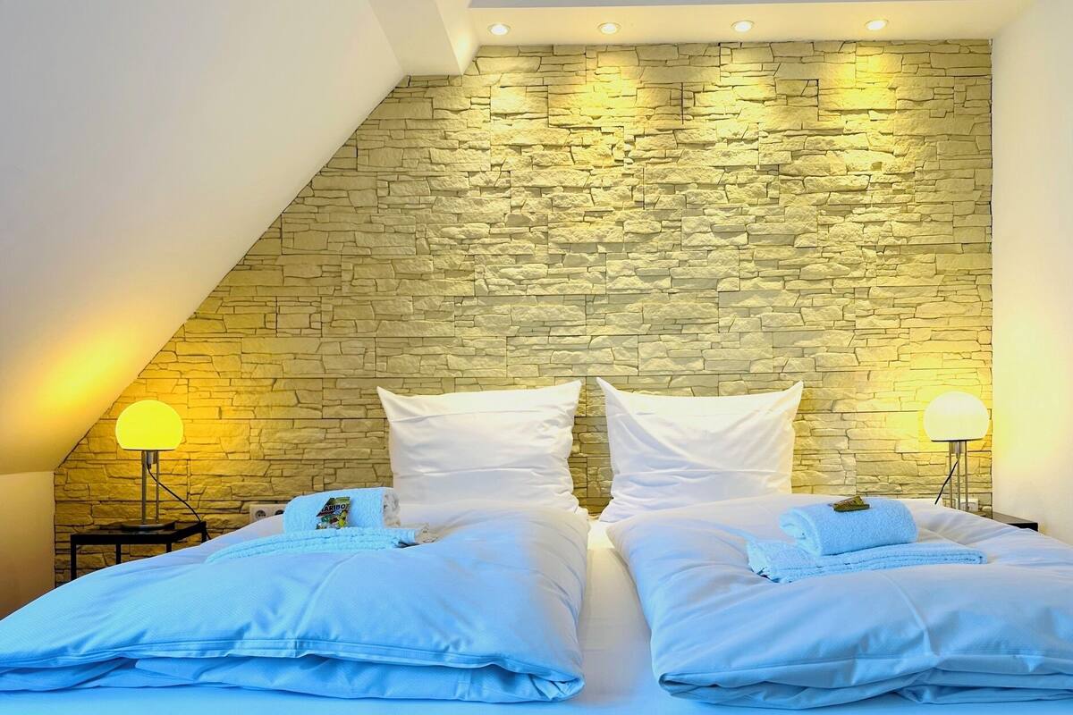 A bedroom with a stone wall, a bed with white bedding, and two bedside lamps.