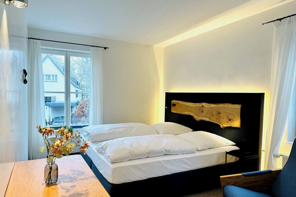 A bedroom with a bed, a chair, a vase with flowers, and a window with curtains.