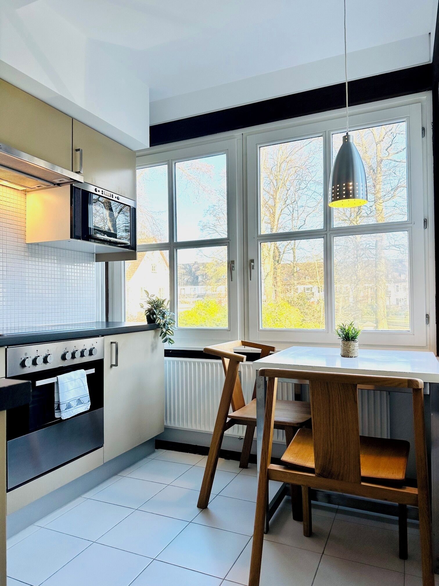 Een moderne keuken met een ingebouwde oven, een eettafel met stoelen, en grote ramen met uitzicht op bomen.