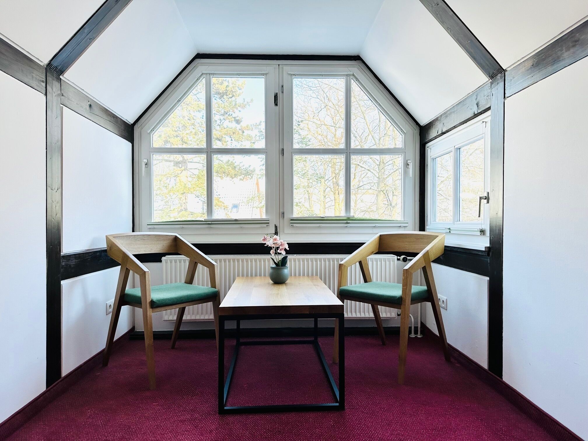Une pièce avec une table et deux chaises, de grandes fenêtres et un radiateur.