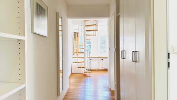 A hallway with wooden flooring, white walls, and a staircase leading to a bright room with windows.