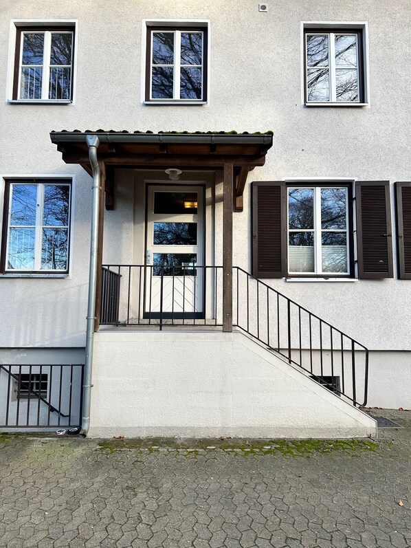 A two-story building with a central entrance, a covered porch, and a staircase leading to the upper floor. - green-man Parkapartments  (Wolfsburg)
