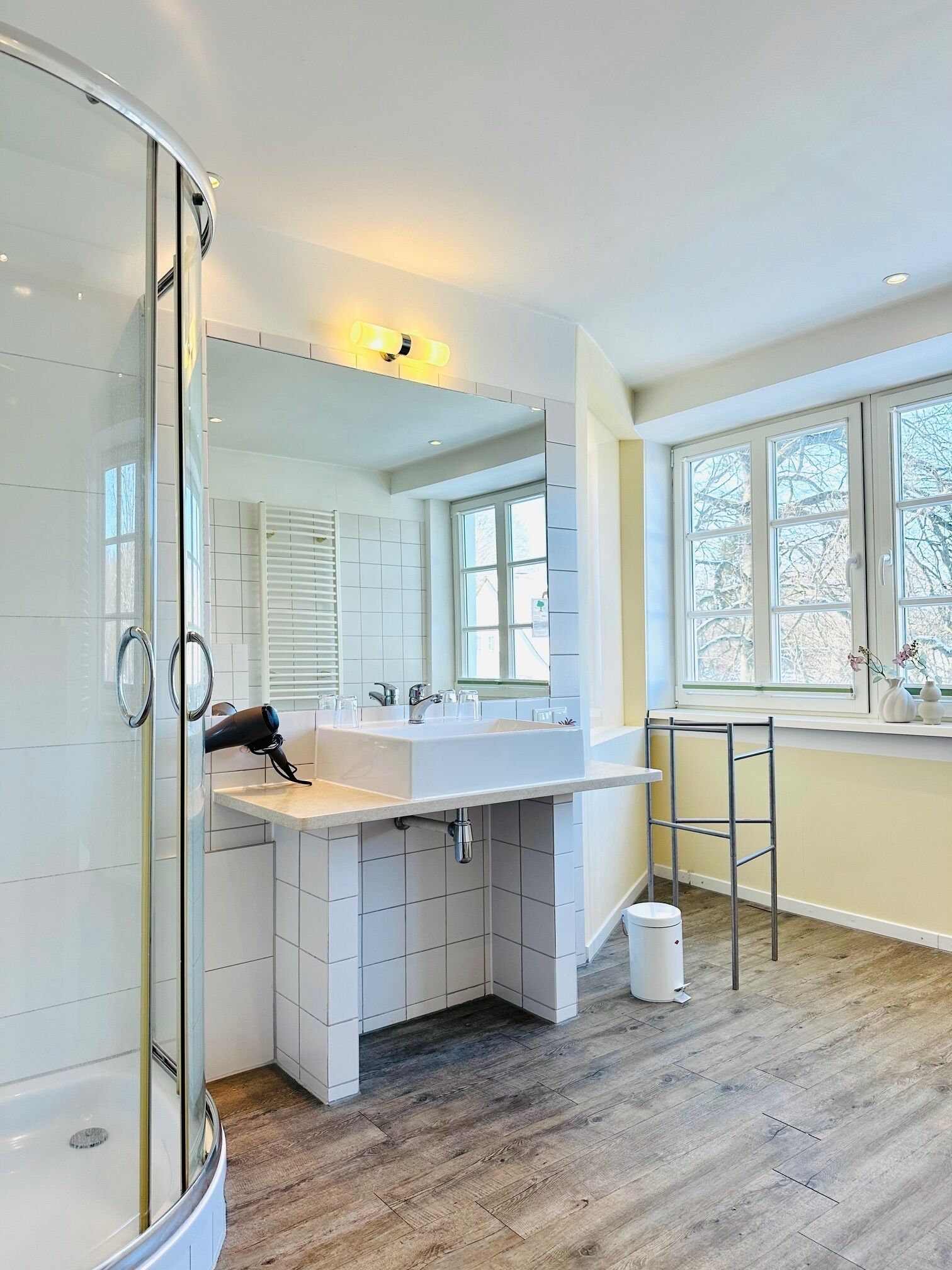 Ein modernes Badezimmer mit Duschkabine aus Glas, einem großen weißen Waschbecken und einem Fenster für natürliches Licht.