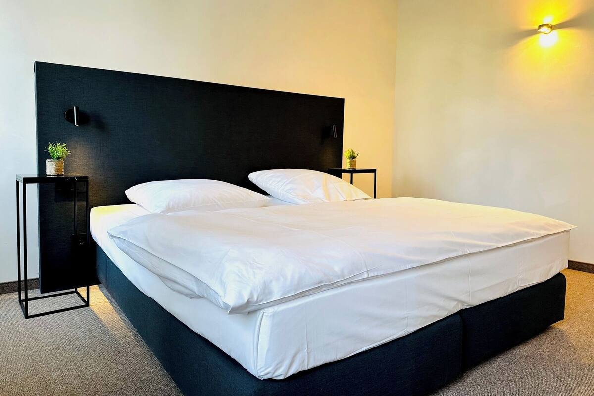 A modern hotel room with a large bed, two bedside tables, and a wall-mounted light fixture.