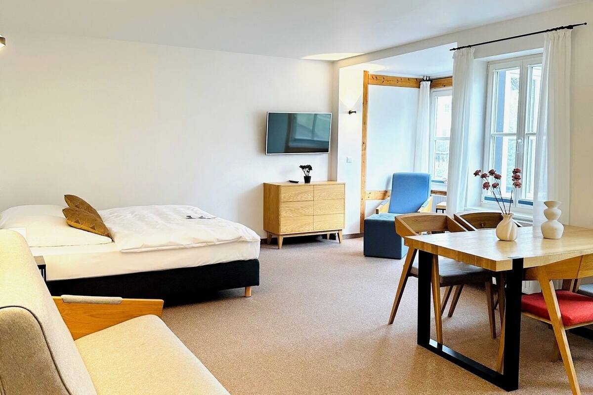 A hotel room with a bed, a sofa, a desk, a TV, a dresser, and a window with curtains.