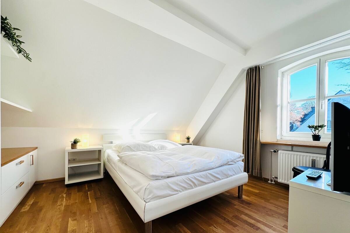 A bedroom with a bed, bedside tables, a window with a view, and a radiator.