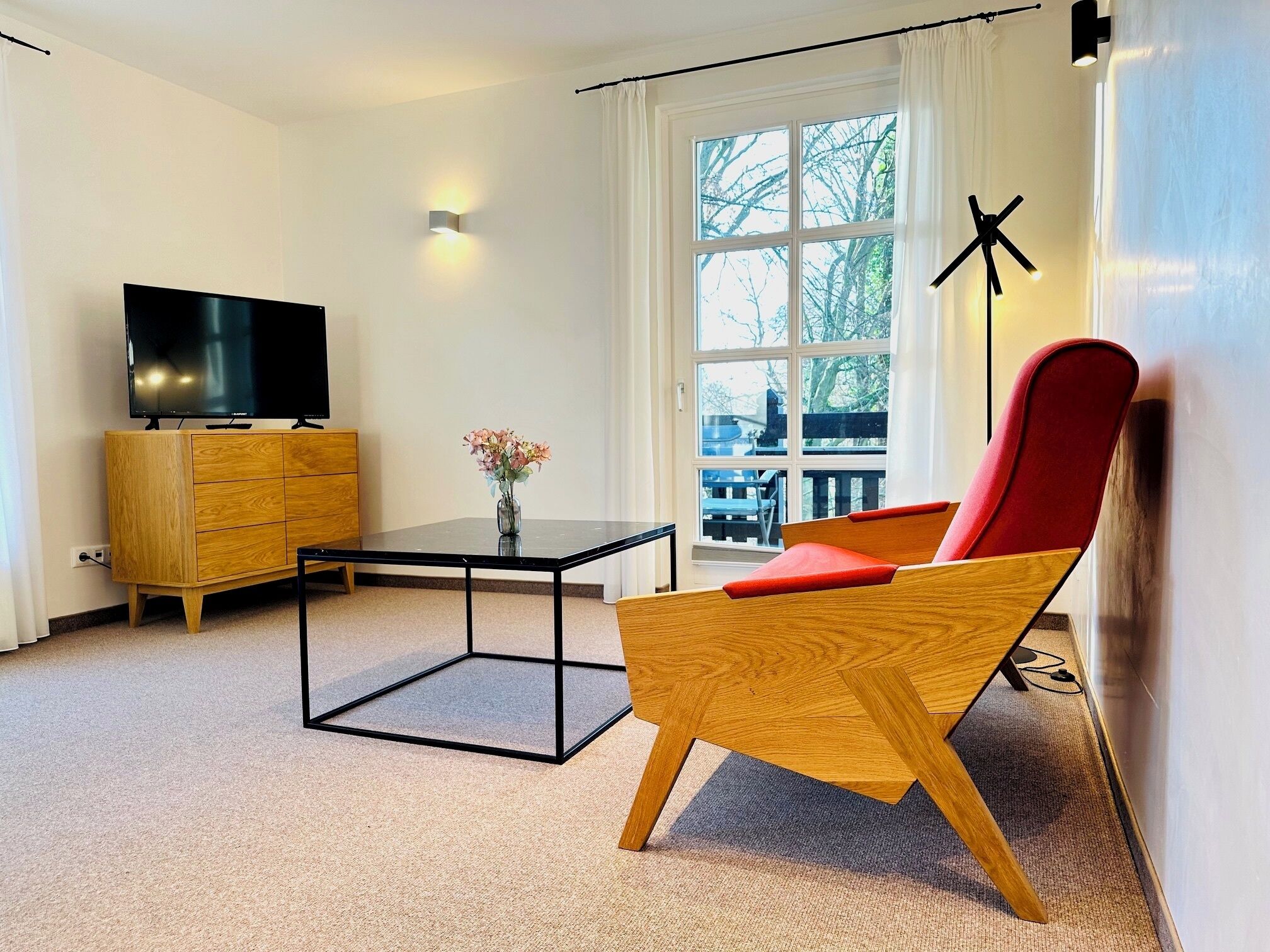 Un salon moderne avec un téléviseur, un meuble en bois et un fauteuil rouge.