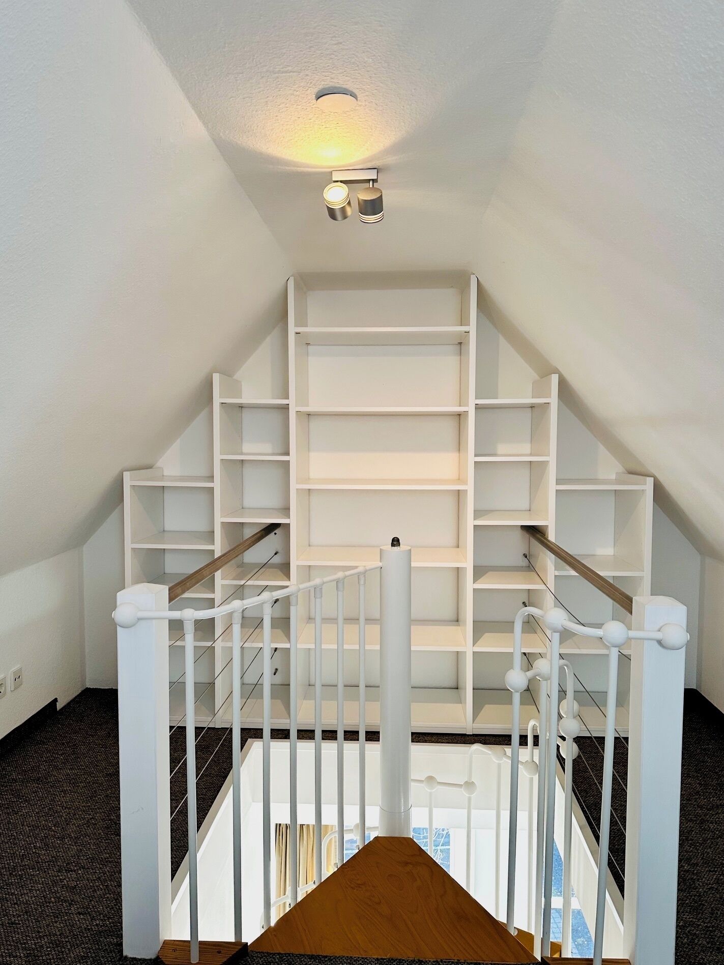 Eine Treppe mit weißen Geländern und einem Holzhandlauf, der zu einer weißen Decke mit Einbuchtungslampen führt.