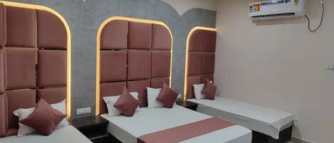 A hotel room with three beds, each with a headboard and pillows. There is a ceiling fan and an air conditioning unit on the wall.