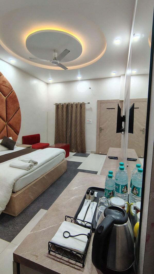 Une chambre d’hôtel avec un lit, une chaise rouge, un bureau, un ventilateur de plafond et un mini-bar.