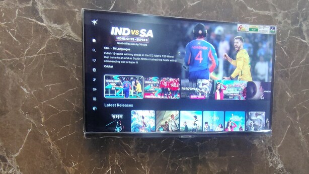 Televisor de pantalla plana montado en una pared de mármol mostrando un partido de cricket entre India y Sudáfrica.