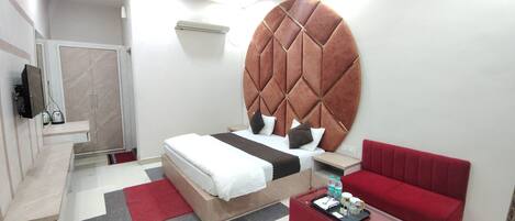 A hotel room with a large bed, a red sofa, a small table with a tray, and a bathroom with a shower and a mirror.