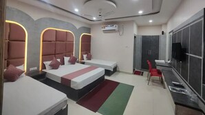 Una habitación de hotel moderna con tres camas, un televisor, un armario y un escritorio.