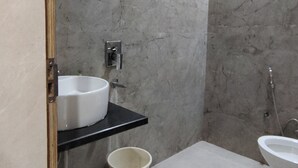 Baño con pared de mármol, lavamanos, inodoro y ducha.