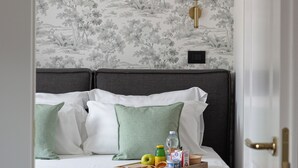Ein ordentlich bezogenes Bett mit Kissen, ein Tablett mit Speisen und Getränken sowie eine Wand mit floralem Muster.