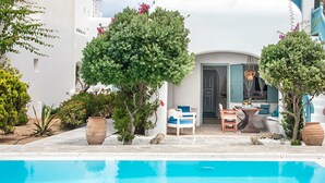Un espace aménagé au bord de la piscine, avec une piscine à l’eau d’un bleu limpide, des meubles d’extérieur blancs et bleus, et des plantes en pot.