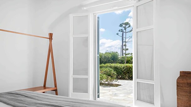 Une chambre avec un lit, une échelle en bois et une vue sur un jardin, visible à travers des portes ouvertes.