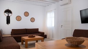 A living room with a brown sofa, a wooden coffee table, and a woven basket on a wooden table. - Mykonos pool house 5 shared pool - My rental Homes (Mykonos)