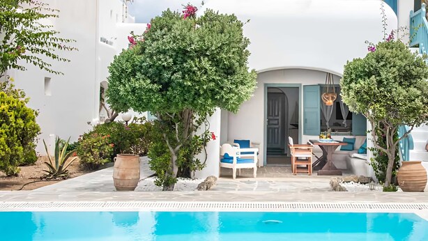 A poolside area with a clear blue pool, white buildings, and a seating area with a table and chairs. - Mykonos pool house 5 shared pool - My rental Homes (Mykonos)