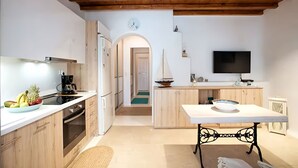 Una cocina moderna con armarios de madera, una estufa y un refrigerador. Hay una mesa de comedor con un cuenco y una pequeña decoración de velero. Un televisor está montado en la pared.
