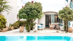Zona de piscina con mobiliario, una puerta que da a una habitación y plantas en macetas.